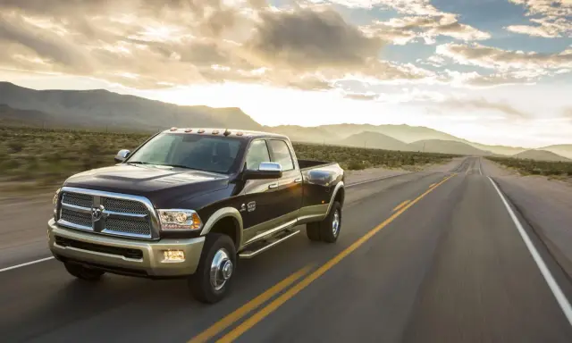 Ciemnobrązowy Dodge Ram 2500 z dwoma rzędami kół jedzie pustynną drogą o zachodzie słońca.