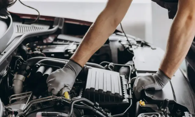 Mechanik w rękawiczkach pracuje przy silniku, dbając o zgodność z normami emisji spalin i tabelą CO2.