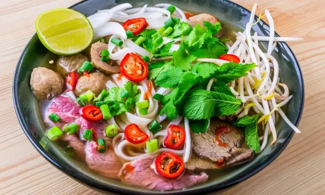 Un bol de soupe pho savoureux avec du bœuf, des boulettes, des nouilles, des herbes fraîches, des piments et un quartier de citron vert.