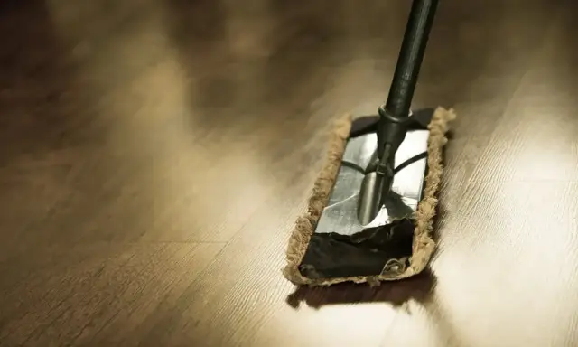 Mop usuwa tłustą plamę po wosku z drewnianej podłogi.