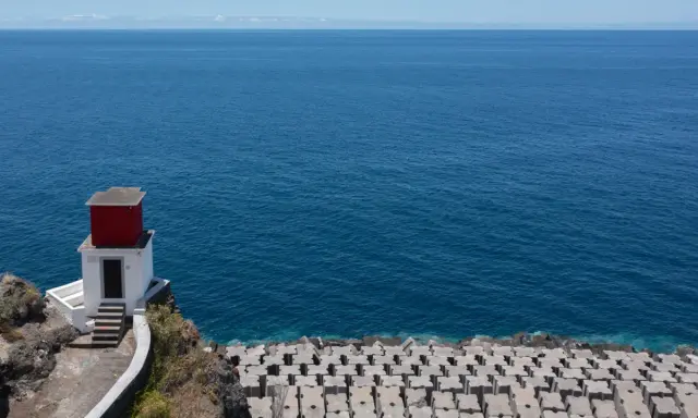 Kleines rotes Haus auf Felsen am Meer bei Ribeira Brava. Wellenbrecher aus Beton säumen die Küste.