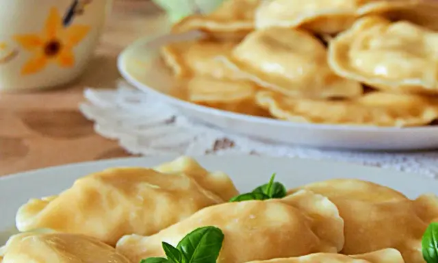 Słowackie pierogi z bryndzą na talerzu, ozdobione listkami bazylii.