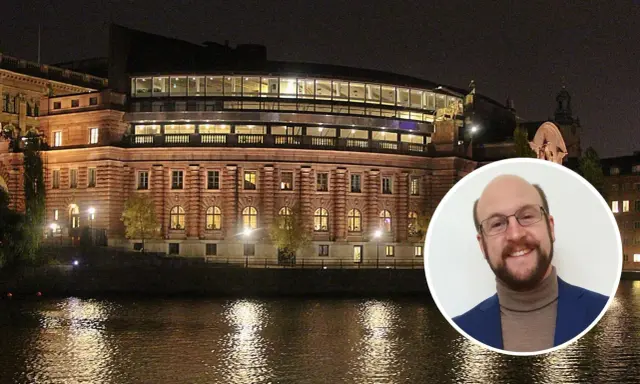 En man ler mot kameran framför Riksdagshuset i Stockholm, en symbol för representativ demokrati.