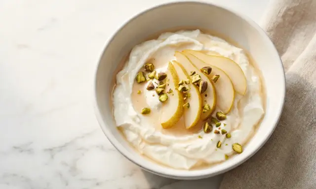 Cremiger Joghurt, der zu lange im Joghurtbereiter war, serviert mit Birnenspalten, Honig und gehackten Pistazien.