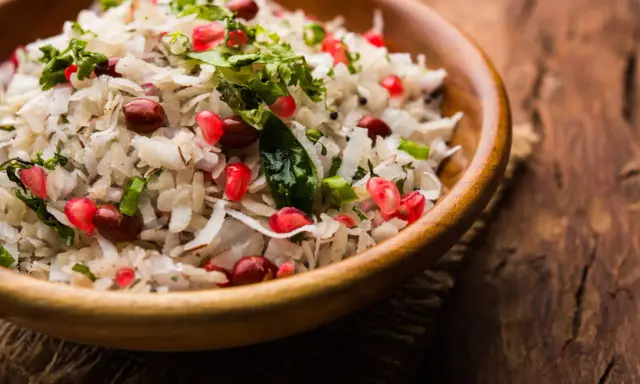 Salade de riz gastronomique, un plat coloré avec des grains de grenade, des cacahuètes et de la coriandre fraîche dans un bol en bois.