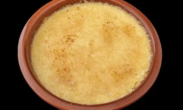 Crème brûlée dans un ramequin en terre cuite, sa surface caramélisée craque sous la cuillère.