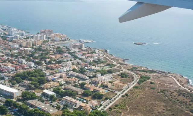 Widok z samolotu na wybrzeże Majorki, z widocznym lotniskiem, miasteczkiem i błękitnym morzem.