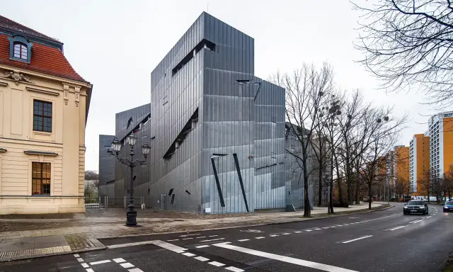 Nowoczesny budynek Muzeum Żydowskiego w Berlinie, obok zabytkowej kamienicy, z charakterystyczną, poszarpaną fasadą.