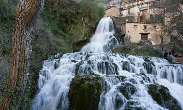 Tosender Wasserfall stürzt über Felsen, Häuser von Orbaneja del Castillo schmiegen sich an den Hang.