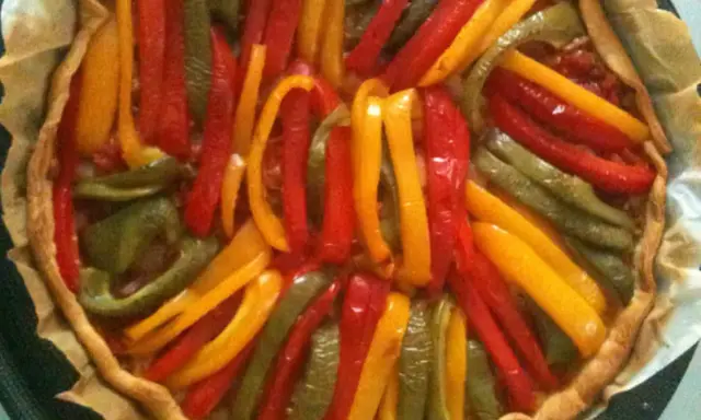 Tarte aux poivrons colorés, un délice visuel et gustatif. Les lanières de poivrons rouges, jaunes et verts forment un motif rayonnant sur la pâte dorée.