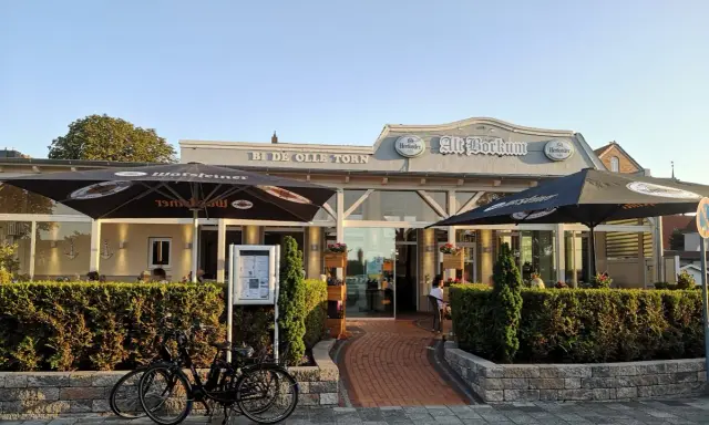Zwei Fahrräder vor dem Restaurant "Alt Borkum" mit Sonnenschirmen und Büschen.
