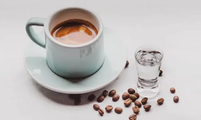 Kawa i alkohol skutki: filiżanka espresso obok kieliszka z wodą i rozsypane ziarna kawy.