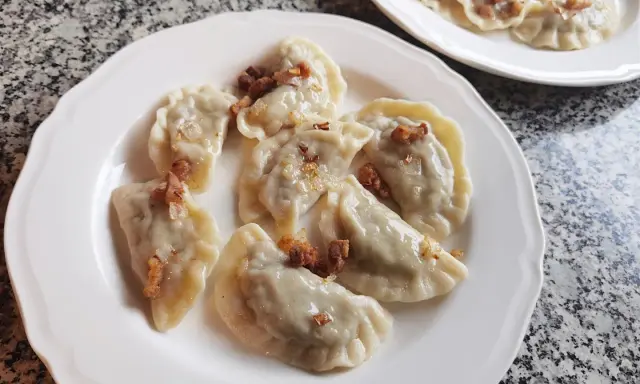 Pyszne pierogi z kapustą i grzybami, posypane skwarkami, na białym talerzu.