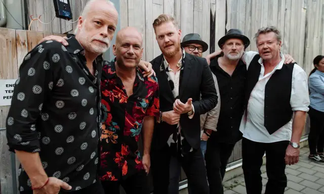 Gruppbild på bandet som är på spåret husband. De står tätt ihop framför en trävägg.