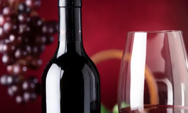 Bouteille de vin rouge connu, verre à vin et grappe de raisins sur fond rouge.
