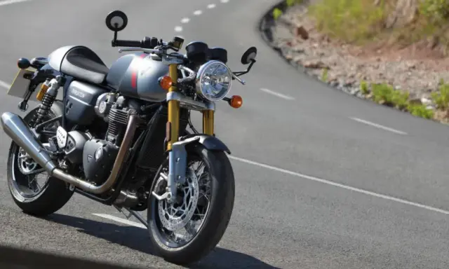 Srebrny Triumph Thruxton 900 na krętej drodze, gotowy na triumfalną jazdę.
