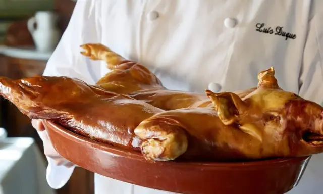 Cochinillo asado, un clásico que comer en Segovia. Un chef presenta este manjar dorado en una cazuela.