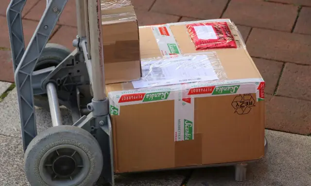 Paczki na wózku, gotowe do wysyłki. Ubezpieczenie paczki DHL to pewność, że dotrze bezpiecznie.