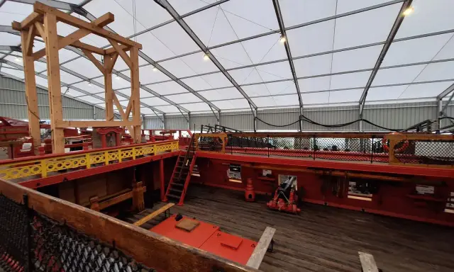L'intérieur du **bateau Hermione** est en cours de restauration. On voit la structure en bois, les ponts rouges et jaunes, et un canon.