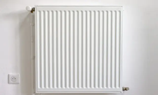 Radiador blanco con termostato, junto a un enchufe. Podría estar haciendo ruido radiador.