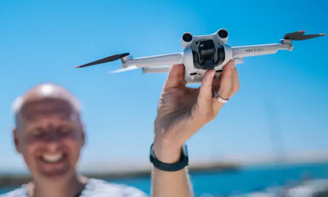 Ręka trzyma drona DJI Mini 3 Pro, gotowego do lotu. Jego imponujący zasięg pozwoli na uchwycenie niesamowitych ujęć.