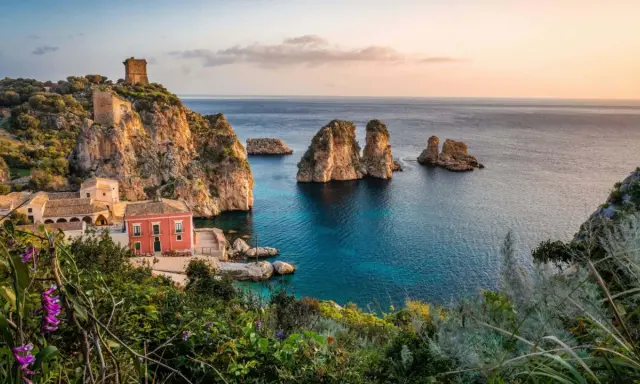 Scopri dove andare in vacanza in Italia: un borgo con torri antiche e faraglioni su un mare cristallino.