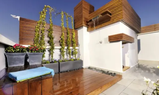 Jardineras de exterior con flores rojas y enredaderas. Un espacio moderno con ducha y terraza de madera.