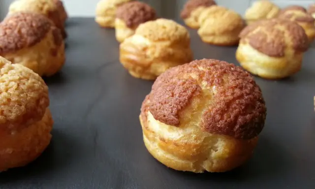 Une rangée de choux craquelins dorés et croustillants, certains avec un dessus brun, prêts à être dégustés.
