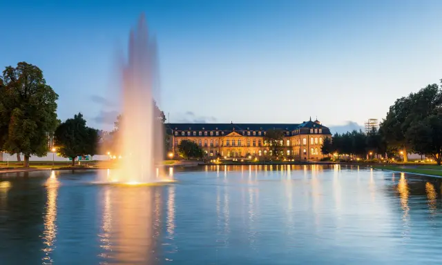 Ein beleuchteter Brunnen spiegelt sich im Wasser vor dem Neuen Schloss in der Stuttgarter Innenstadt.