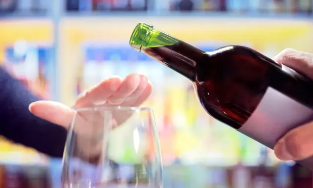 Hand stoppt Weinglas, während eine Flasche Rotwein eingegossen wird. Ein Symbol für bewussten Weinkonsum weltweit.