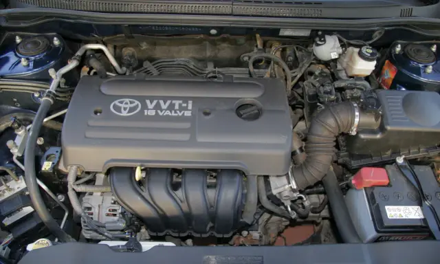 Silnik VVT-i 16 Valve z Toyoty Corolla E12. Widoczny alternator, akumulator i elementy układu dolotowego.