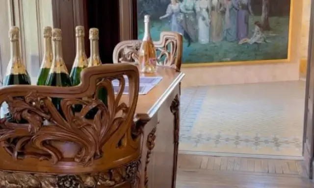 Bouteilles de champagne sur un meuble sculpté dans la maison Demoiselle à Reims. Un tableau orne le mur.