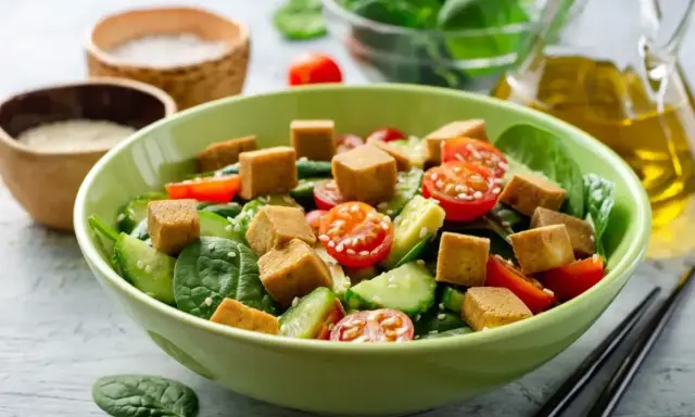 Pyszna sałatka z tofu, pomidorkami koktajlowymi, ogórkiem i szpinakiem, posypana sezamem. Idealna na lekki posiłek.