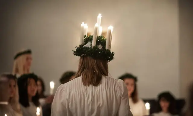 En flicka med ljuskrona bär fram ett lucia namn. Hon leder en procession av flickor med ljus i mörkret.