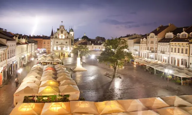 Nocny rzeszów rynek podczas burzy z piorunami. Mokry bruk, oświetlone kamienice i ogródki restauracyjne pod namiotami tworzą magiczny klimat.