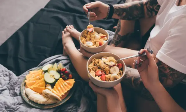Para jedząca płatki z owocami i talerz świeżych owoców na łóżku. Zdrowy początek dnia, czyli zbilansowana dieta.