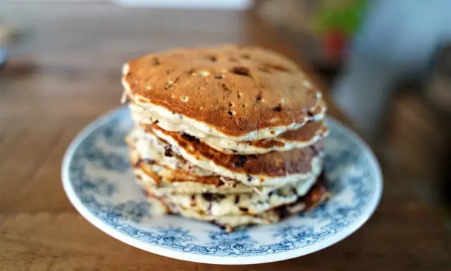 Pile de pancakes pepite chocolat sur une assiette bleue et blanche, prêts à être dégustés.