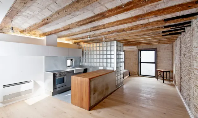 Cocina moderna con isla de madera y cristal, techos de vigas expuestas. Un espacio abierto que evoca la idea de como tirar un tabique para crear amplitud.