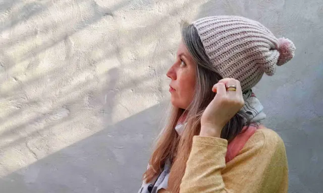Mujer con gorro tejido a crochet, con pompón rosa. Disfruta del proceso de tejer gorros crochet.