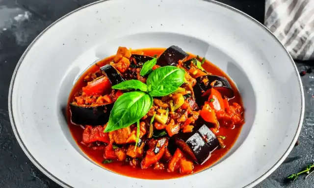 Un plat de ratatouille recette coloré et appétissant, garni de basilic frais, dans une assiette blanche.