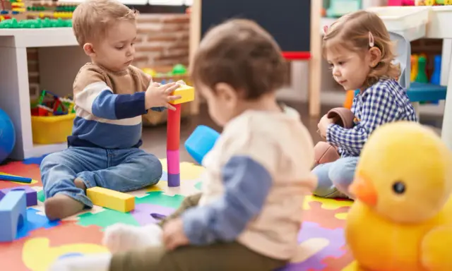 Trójka małych dzieci bawi się klockami i zabawkami na kolorowej macie w żłobku.