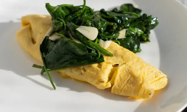 Złożony omlet francuski z zielonym szpinakiem i czosnkiem na białym talerzu.