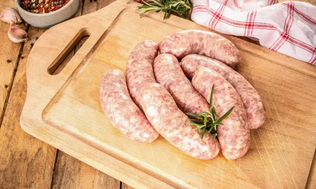 Surowe kiełbaski na desce, obok gałązka rozmarynu. Zastanawiasz się, jak długo można mrozić kiełbasę, by zachowała świeżość?