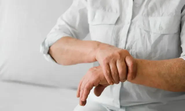 Osoba w białej koszuli masuje nadgarstek, odczuwając ból stawów rąk i nóg.