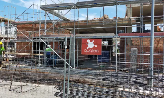 Obra en construcción con andamios y ladrillos. Se ve el logo de "qualee". ¿Cuánto se tarda en construir un edificio de 7 plantas?