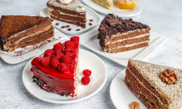 Variedad de pasteles en una mesa: uno de chocolate con cacao, otro con glaseado rojo y frambuesas, y uno con nueces. Una deliciosa carta de postres.