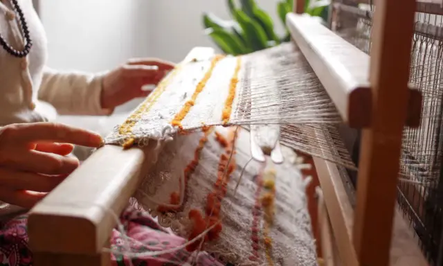 Hands weave a textured fabric on a loom, a beautiful example of textile upcycling.