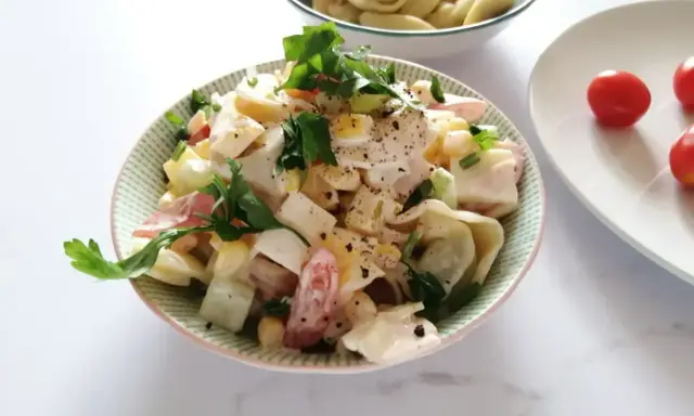 Pyszna sałatka z tortellini, jajka, kukurydzy i pomidorów, udekorowana natką pietruszki. Idealna na letnie dni.