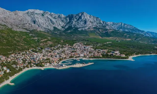 Widok na Baśkę Vodę z górami w tle. Atrakcje turystyczne obejmują plaże, port jachtowy i urokliwe miasteczko.