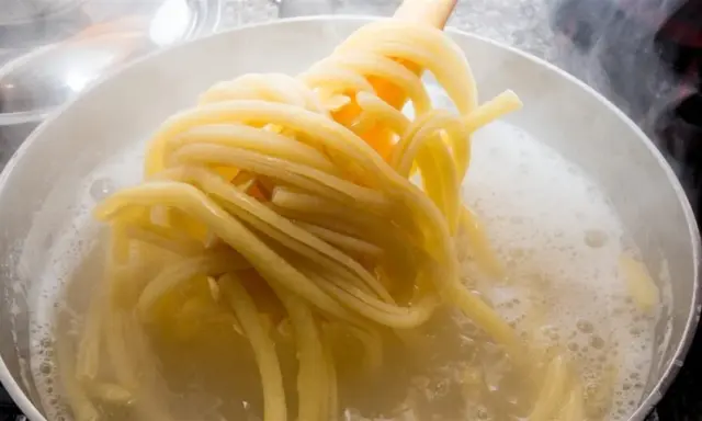 Gorący garnek z bulgoczącą wodą, z którego wyciągane są idealne, sprężyste nitki makaronu al dente.